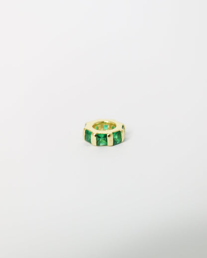 Gold ring with green gemstones on a light gray background