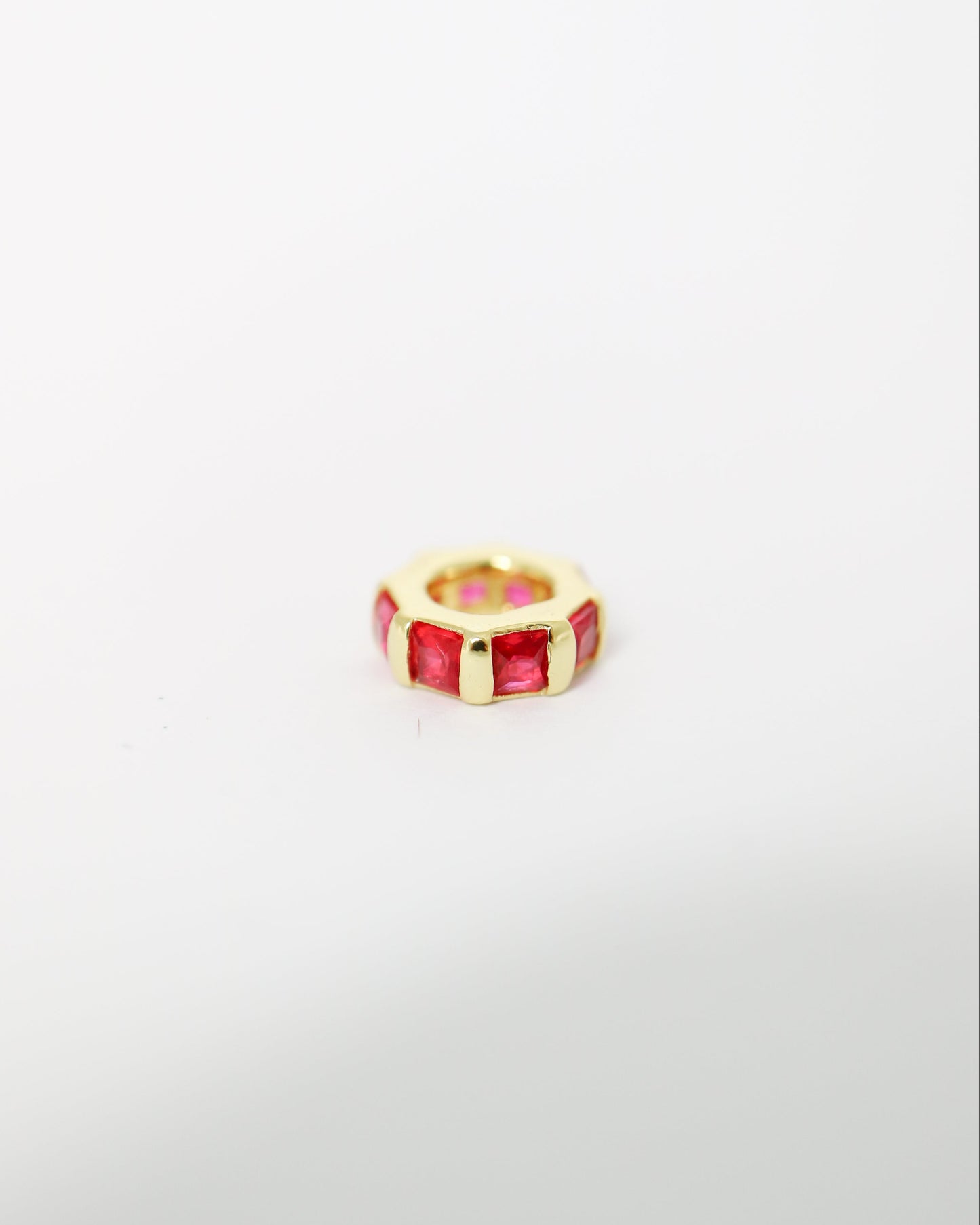 Gold ring with red gemstone on a light gray background