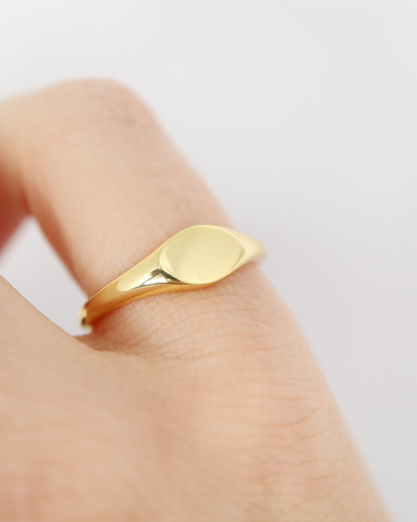 Gold ring on a finger against a light background