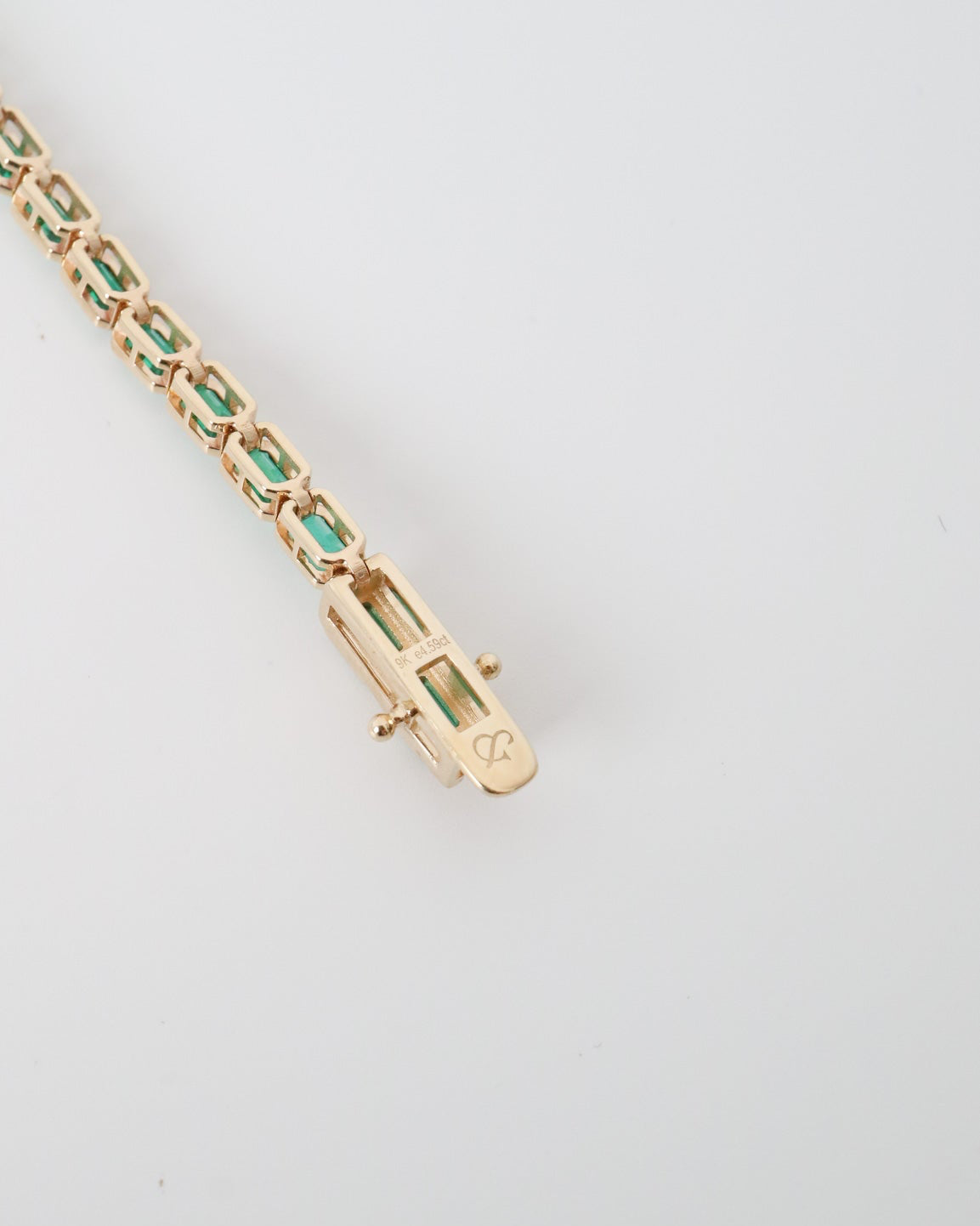 Gold bracelet with green gemstones on a light gray background