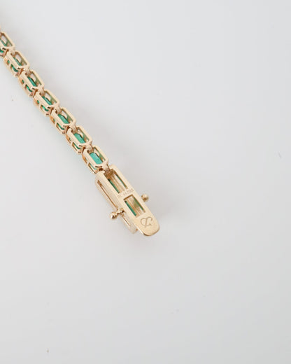 Gold bracelet with green gemstones on a light gray background