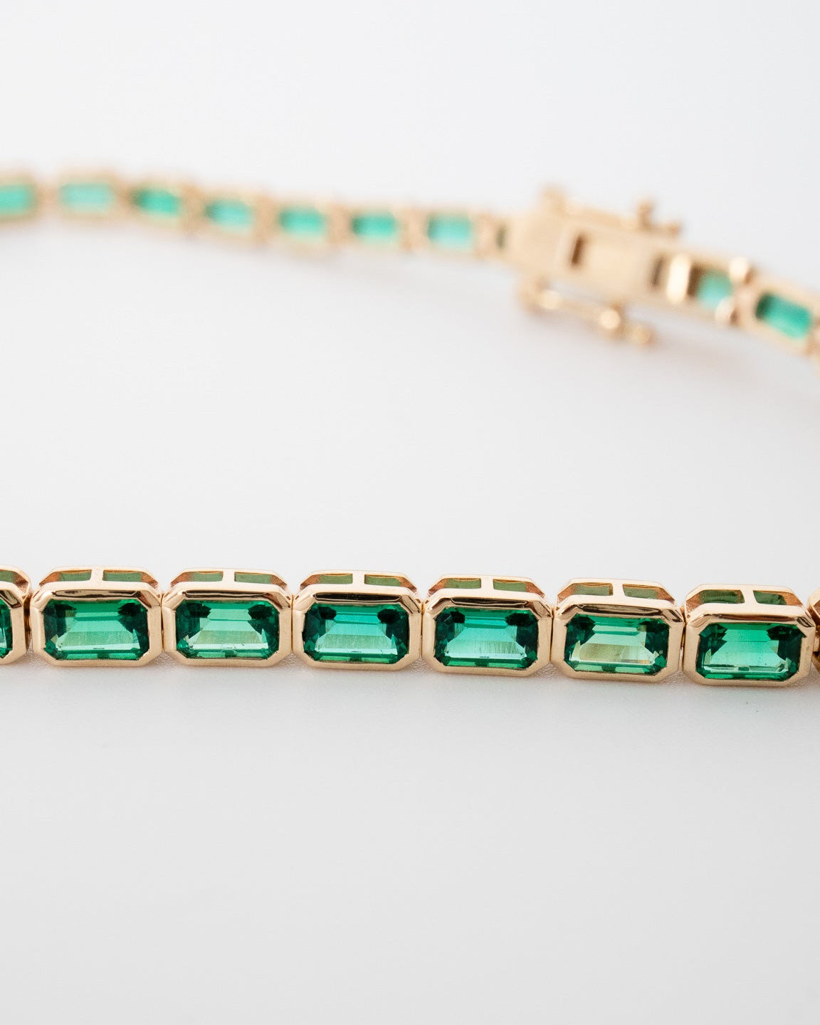 Rose gold bracelet with green gemstones on a light gray background