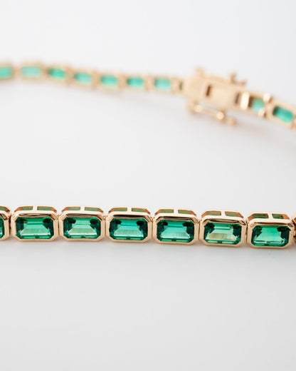 Rose gold bracelet with green gemstones on a light gray background