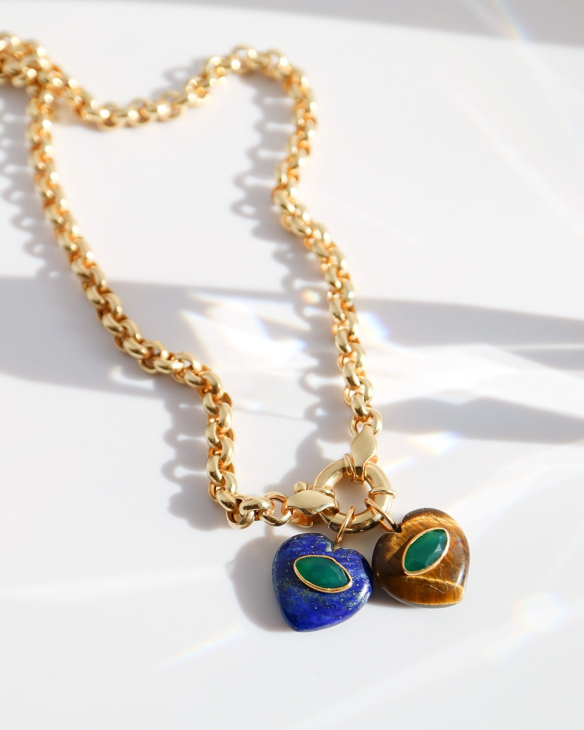 Gold necklace with heart-shaped blue and green charms on a white background