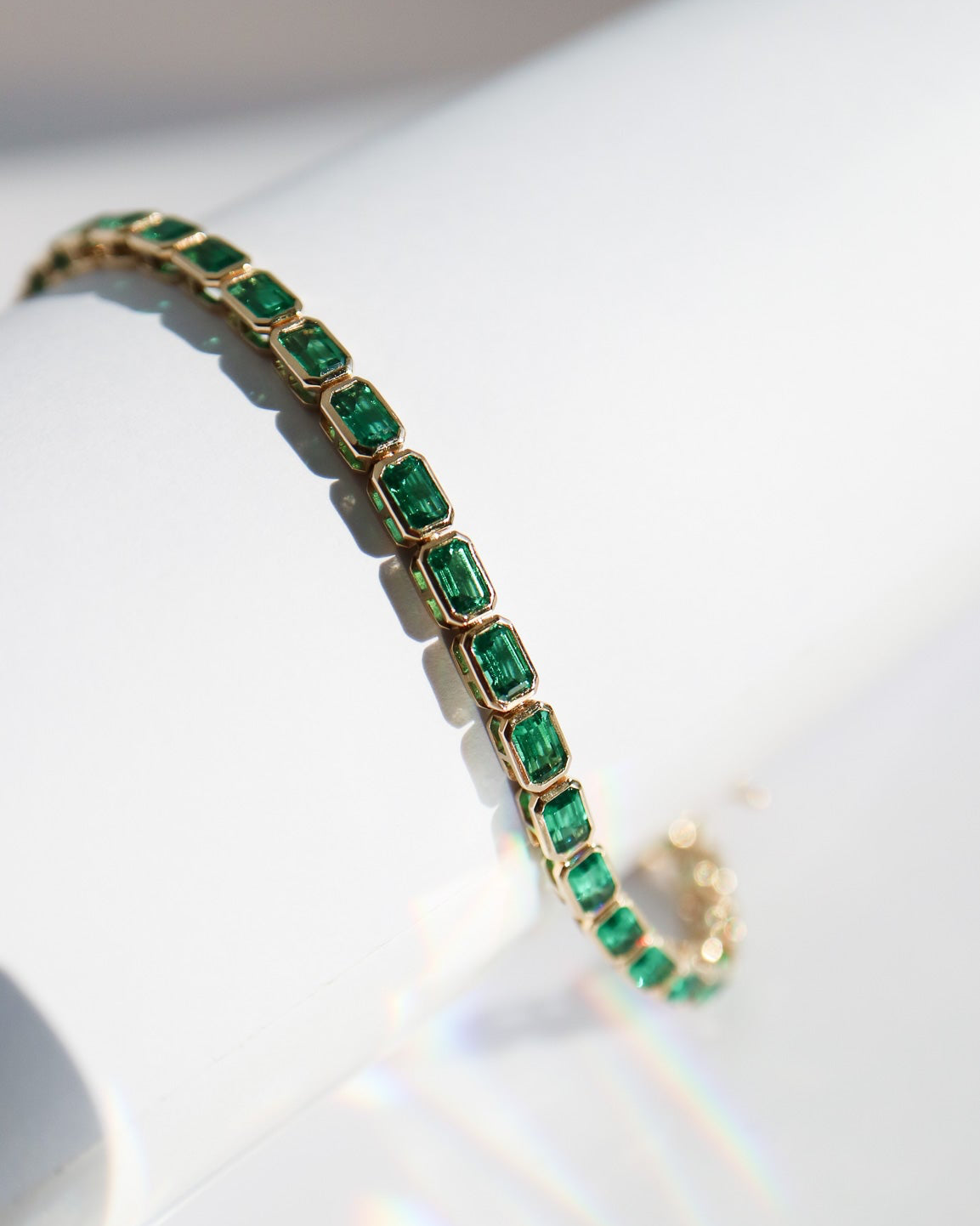 Gold bracelet with green gemstones on a white stand