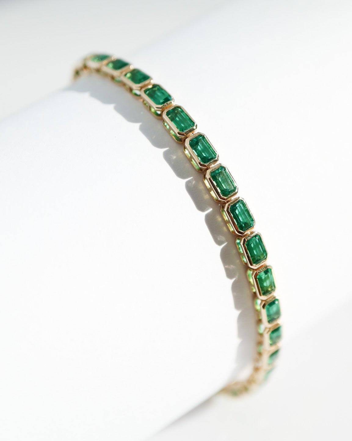 Gold bracelet with green gemstones on a white background