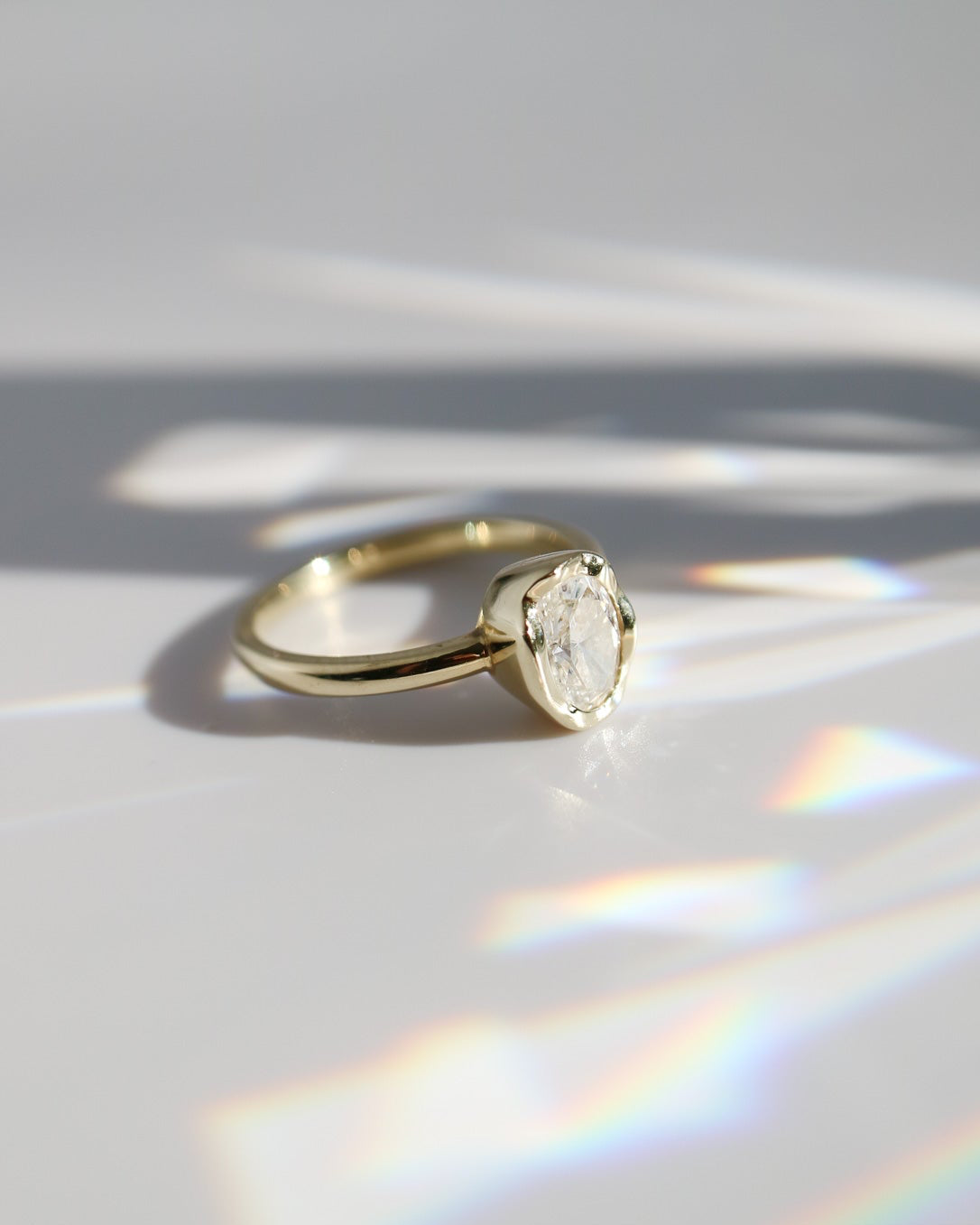 Gold ring with a diamond on a white surface with rainbow reflection