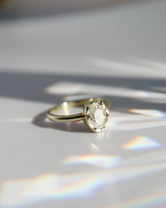Gold ring with a diamond on a reflective surface with rainbow colors.