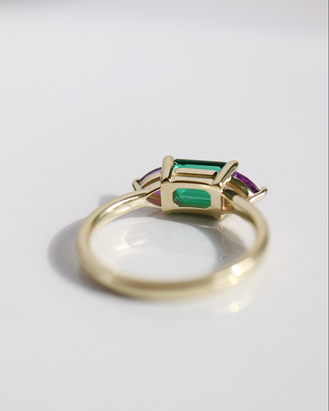 Gold ring with green and red gemstones on a light gray background