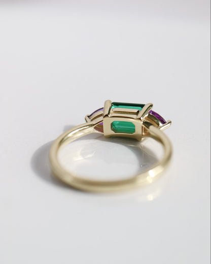 Gold ring with green and red gemstones on a light gray background