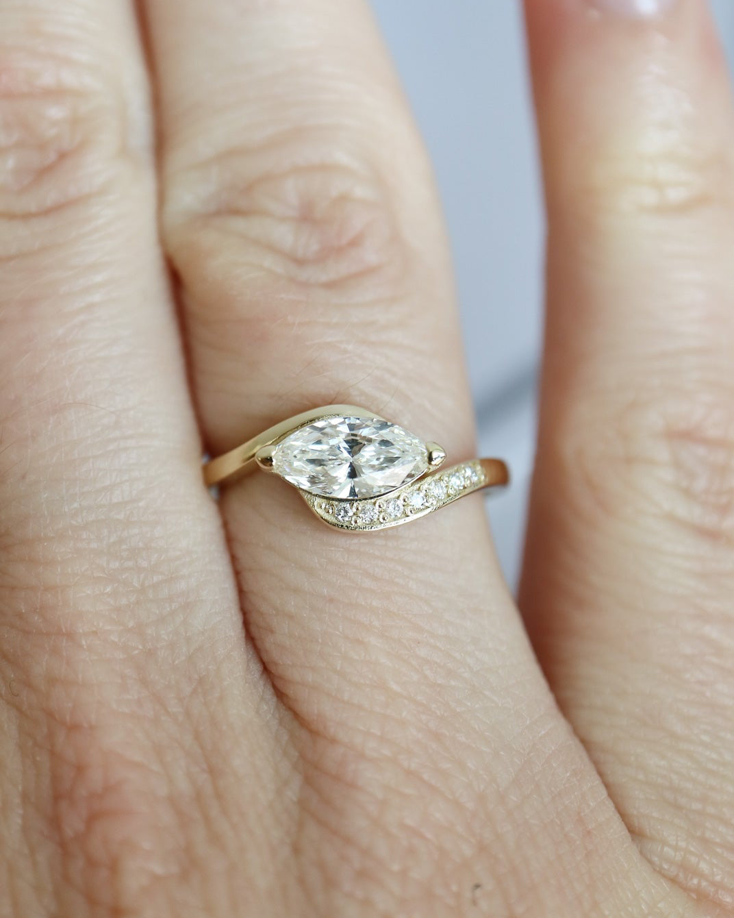 Gold ring with a diamond on a finger against a neutral background