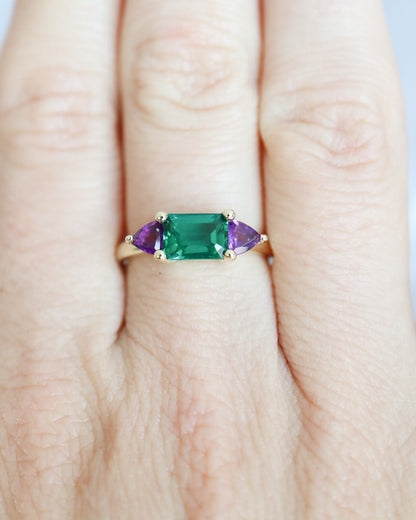 Ring with green and purple gemstones on a finger against a light background