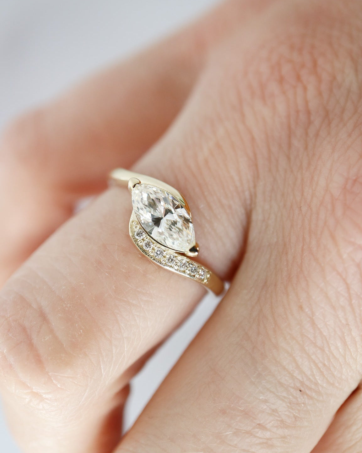 Gold ring with a pear-shaped diamond on a finger against a light background