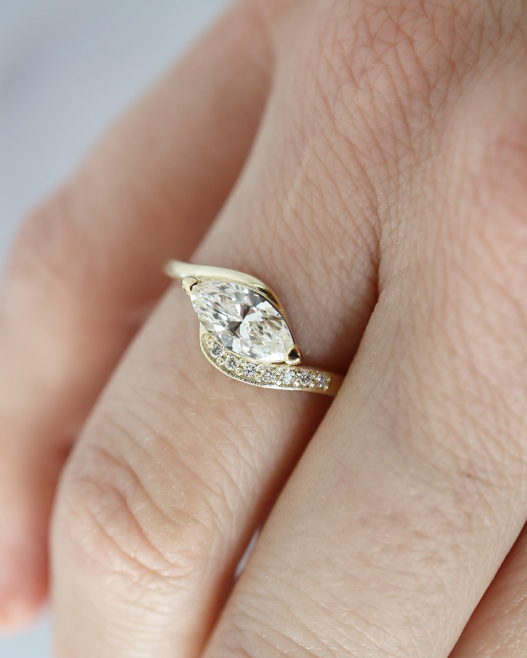 Gold ring with a diamond on a person's finger against a neutral background