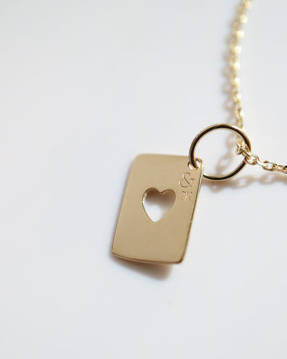Gold necklace with a rectangular tag featuring a heart cutout on a white background