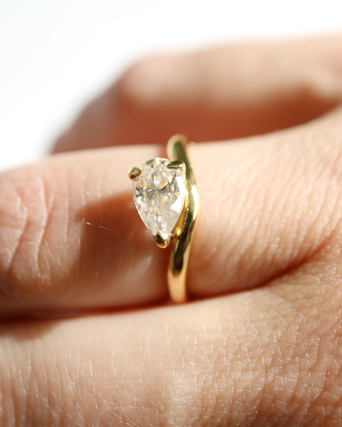 Gold ring with a pear-shaped diamond on a finger against a blurred background