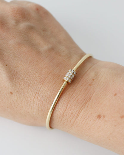 A gold bangle bracelet with a small pavé-set diamond accent, shown worn on a person's wrist against a light gray background.