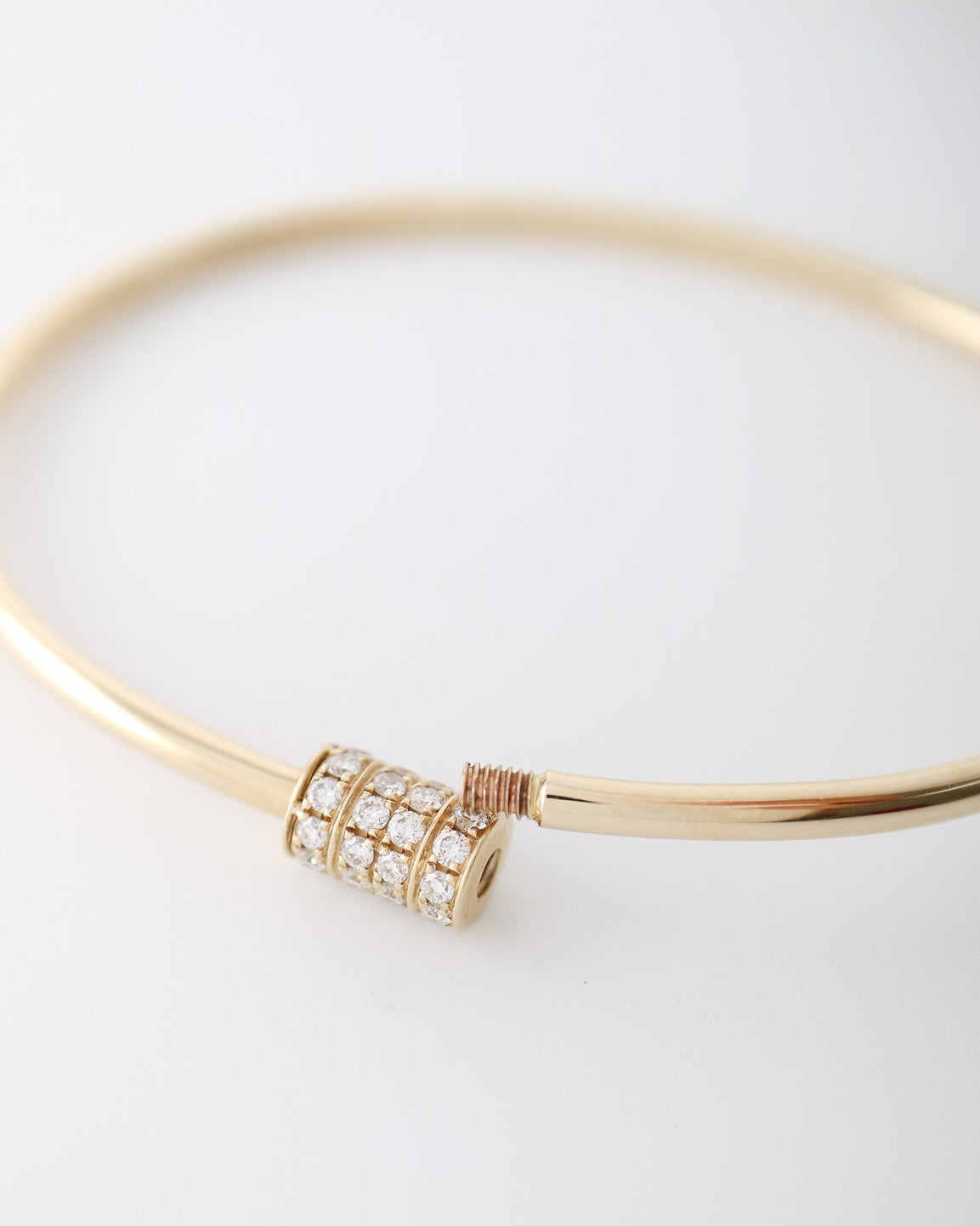 A 14kt gold bangle bracelet featuring a central cylindrical charm paved with clear diamonds and accented with a small rose gold wrap, shown on a clean white background.