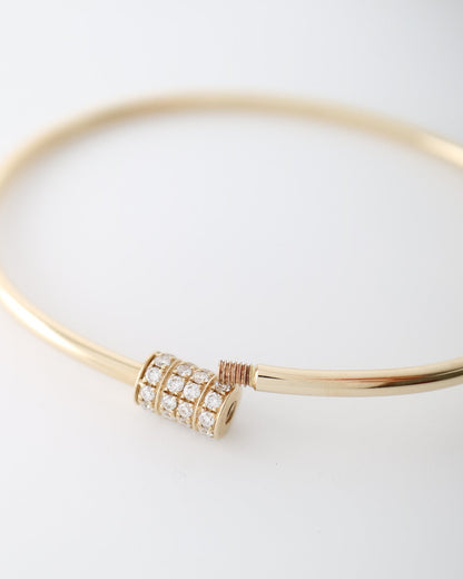 A 14kt gold bangle bracelet featuring a central cylindrical charm paved with clear diamonds and accented with a small rose gold wrap, shown on a clean white background.