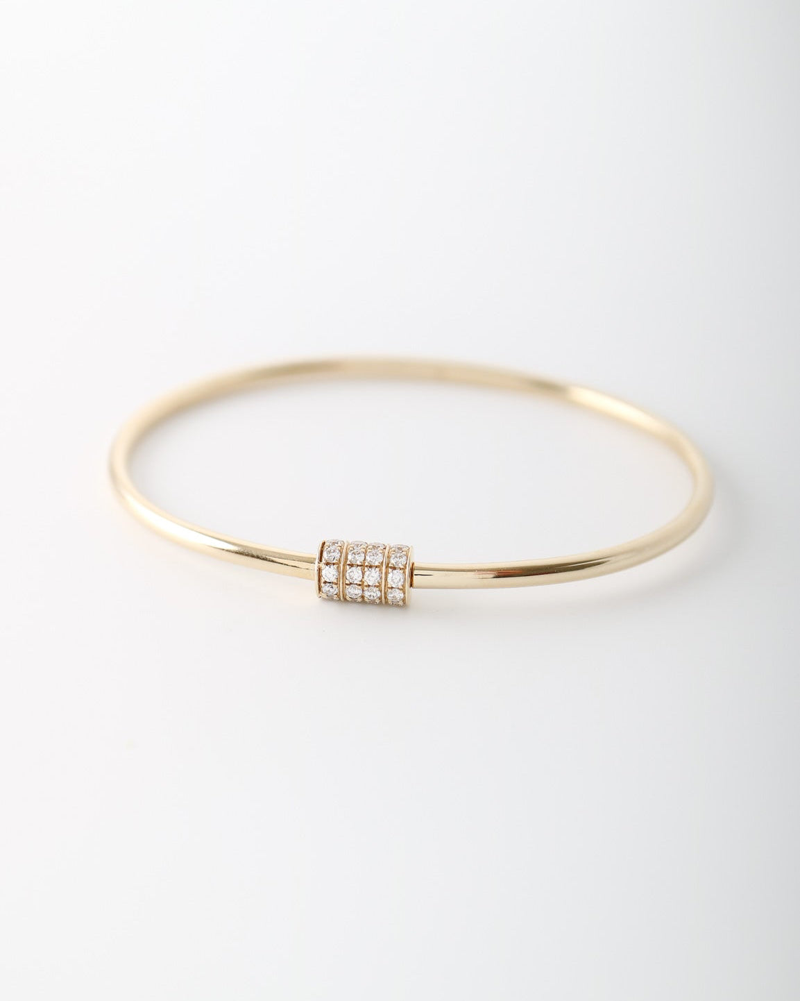 A thin gold bangle bracelet with a central cylindrical cluster of small clear stones, photographed on a clean white background.
