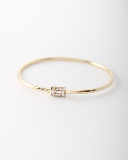 A thin gold bangle bracelet with a central cylindrical cluster of small clear stones, photographed on a clean white background.