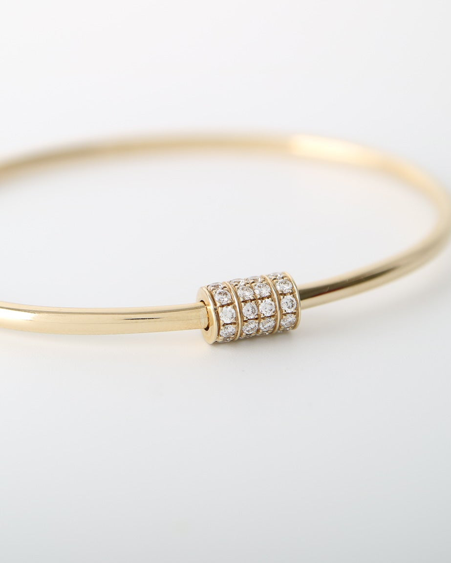 A thin yellow gold bangle bracelet with a small cylindrical bezel-set cluster of clear stones at the front, photographed on a clean white background.