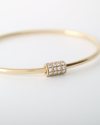 A thin yellow gold bangle bracelet with a small cylindrical bezel-set cluster of clear stones at the front, photographed on a clean white background.