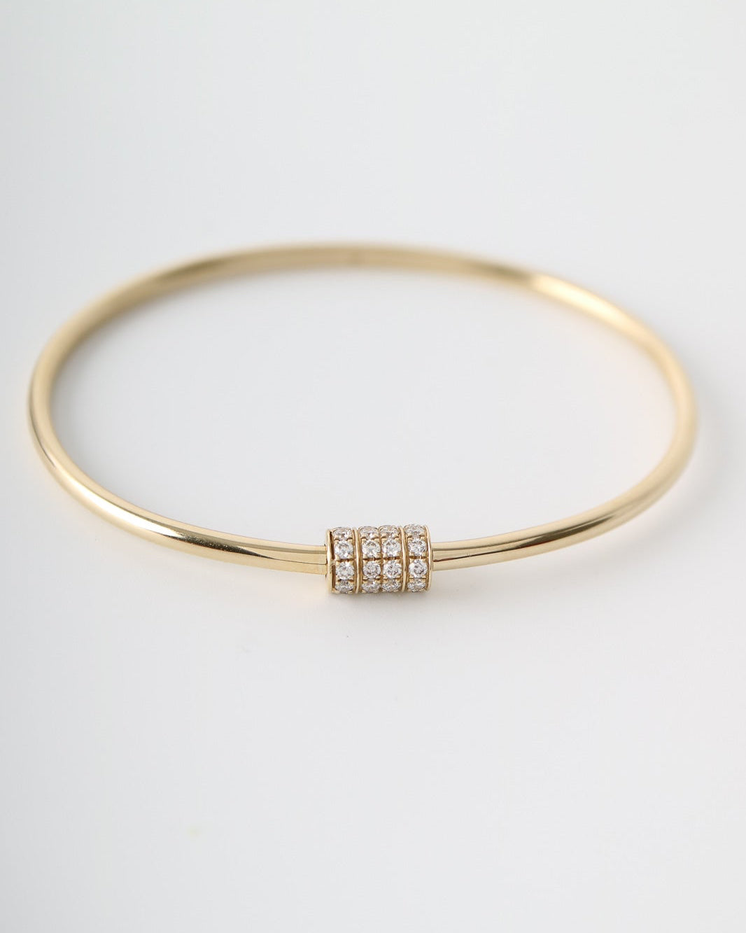A thin gold bangle bracelet with a small rectangular cluster of clear pavé stones at the center, photographed on a clean white background.