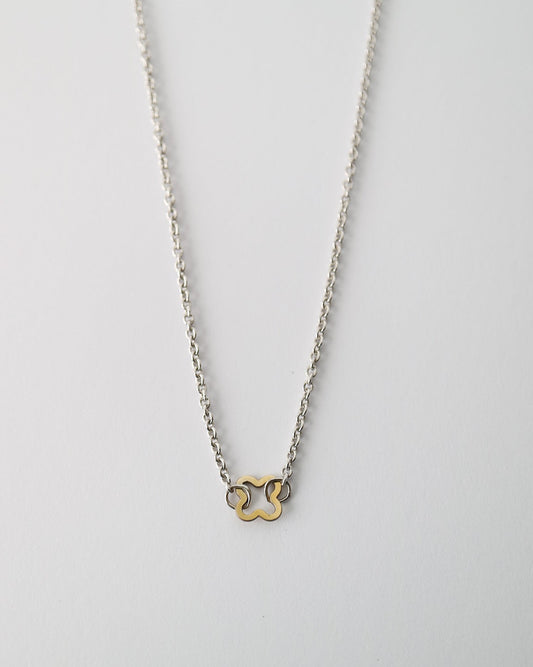 A delicate silver chain necklace featuring a small, minimalist gold-tone double-ring pendant, displayed against a clean, light gray background.