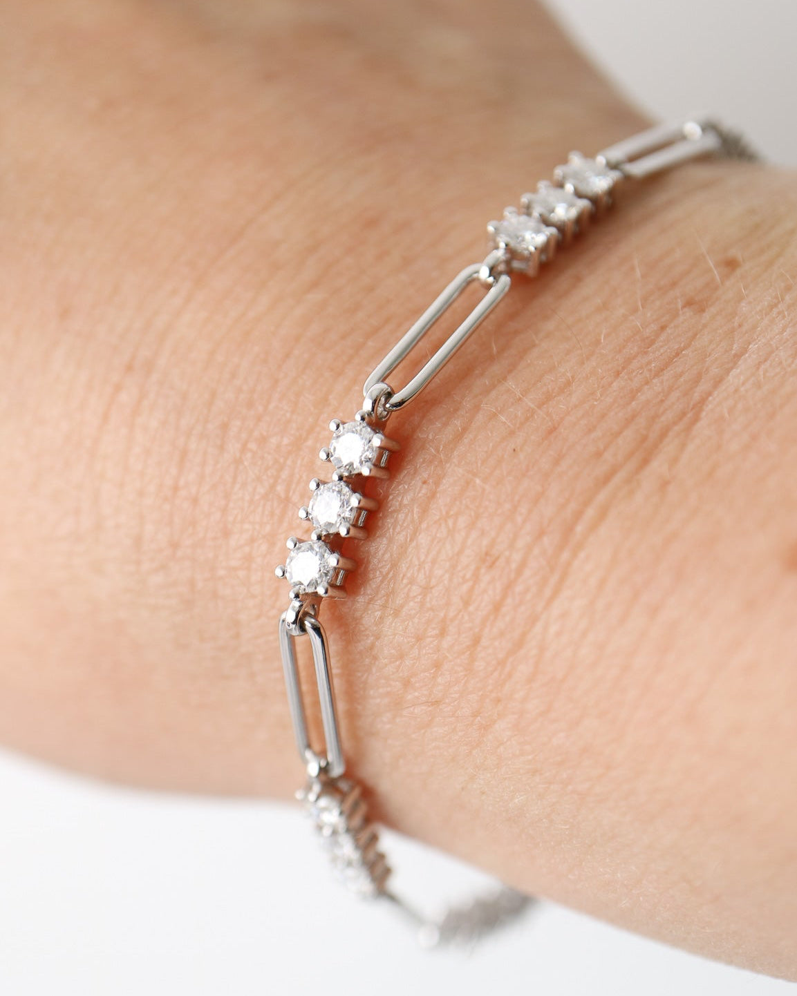 A silver-toned link bracelet with clear round-cut stones, shown worn on a person's wrist against a plain light background.