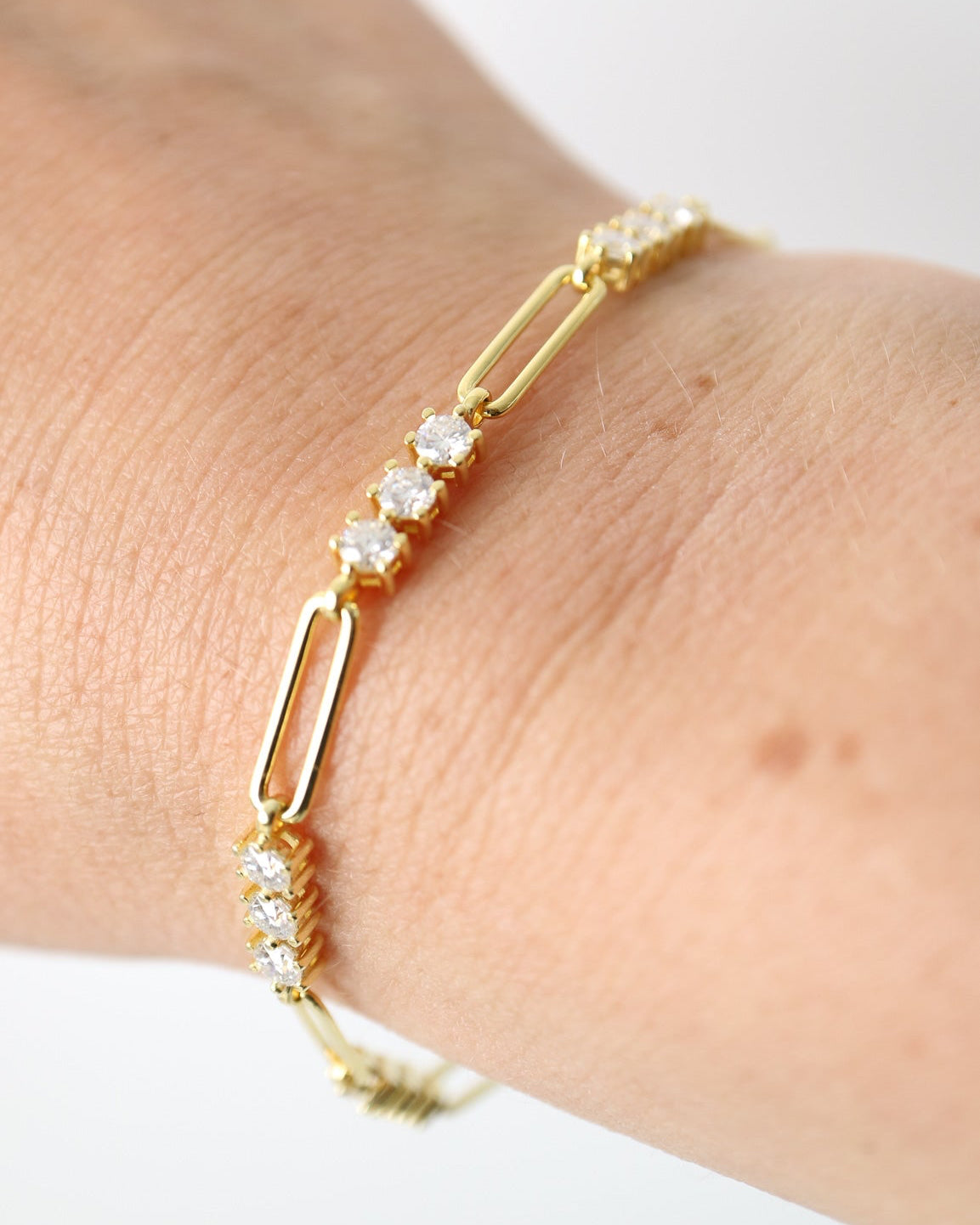A delicate gold link bracelet with clear cubic zirconia stones, shown worn on a person's wrist against a plain white background.