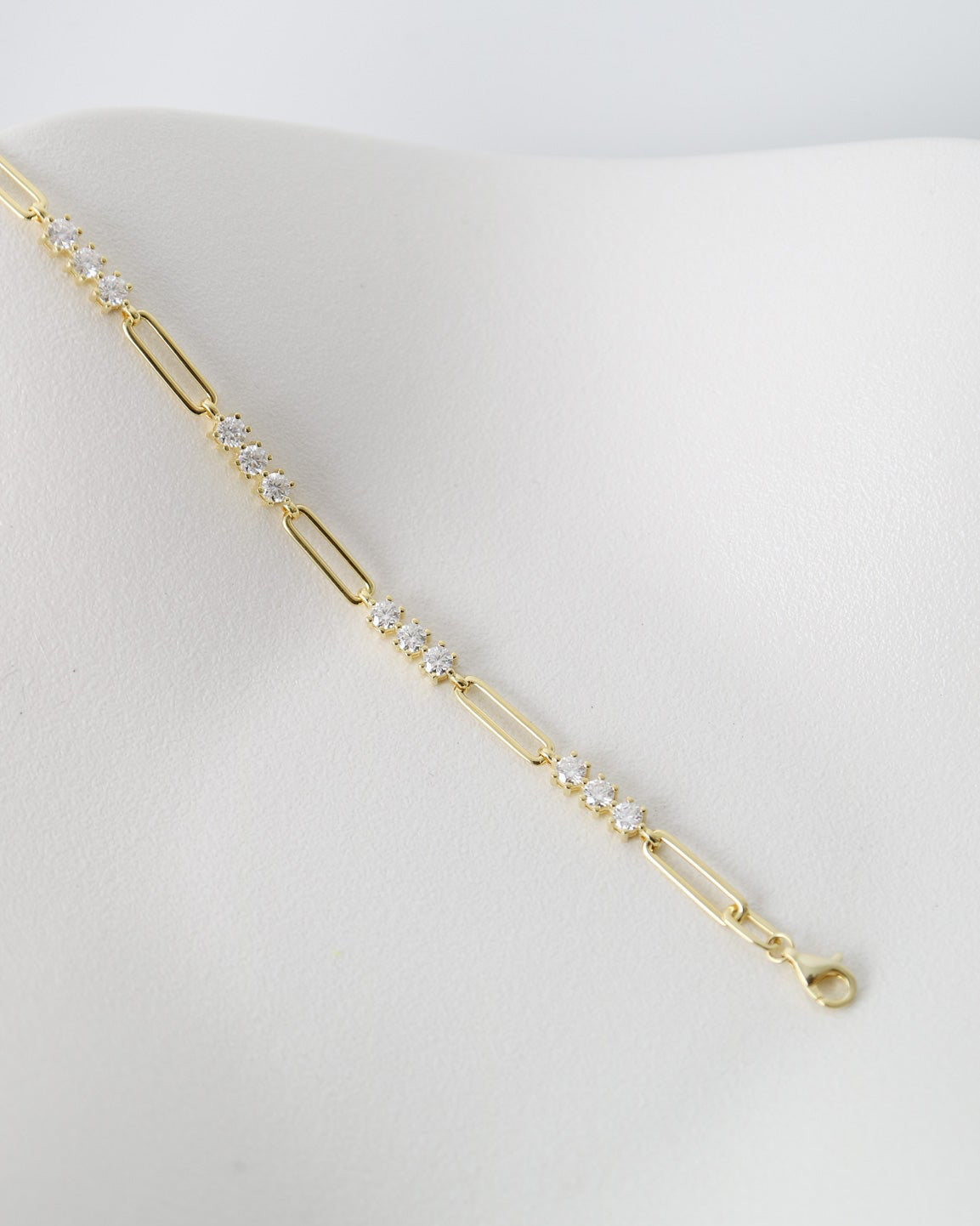 A delicate gold paperclip chain bracelet with small clear crystal accents, displayed on a white jewelry bust against a light gray background.