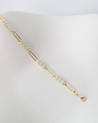 A delicate gold paperclip chain bracelet with small clear crystal accents, displayed on a white jewelry bust against a light gray background.