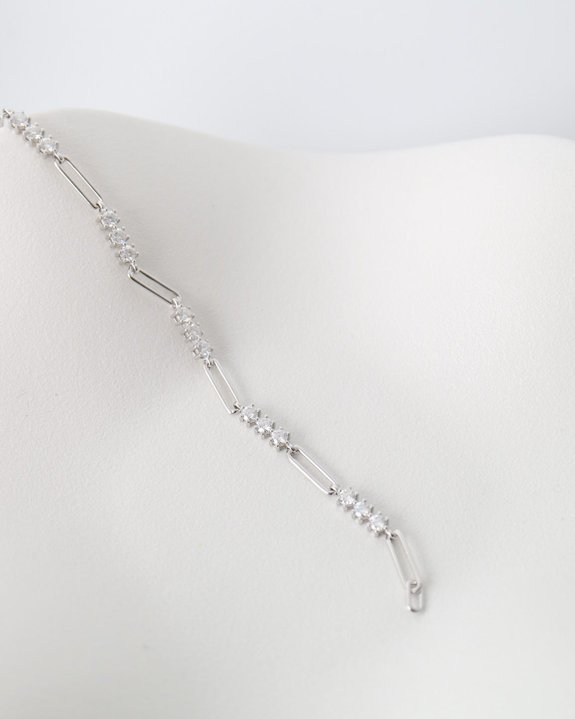 A delicate silver-toned chain necklace with small clear stones, draped on a white display bust against a light gray background.