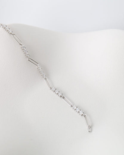 A delicate silver-toned chain necklace with small clear stones, draped on a white display bust against a light gray background.