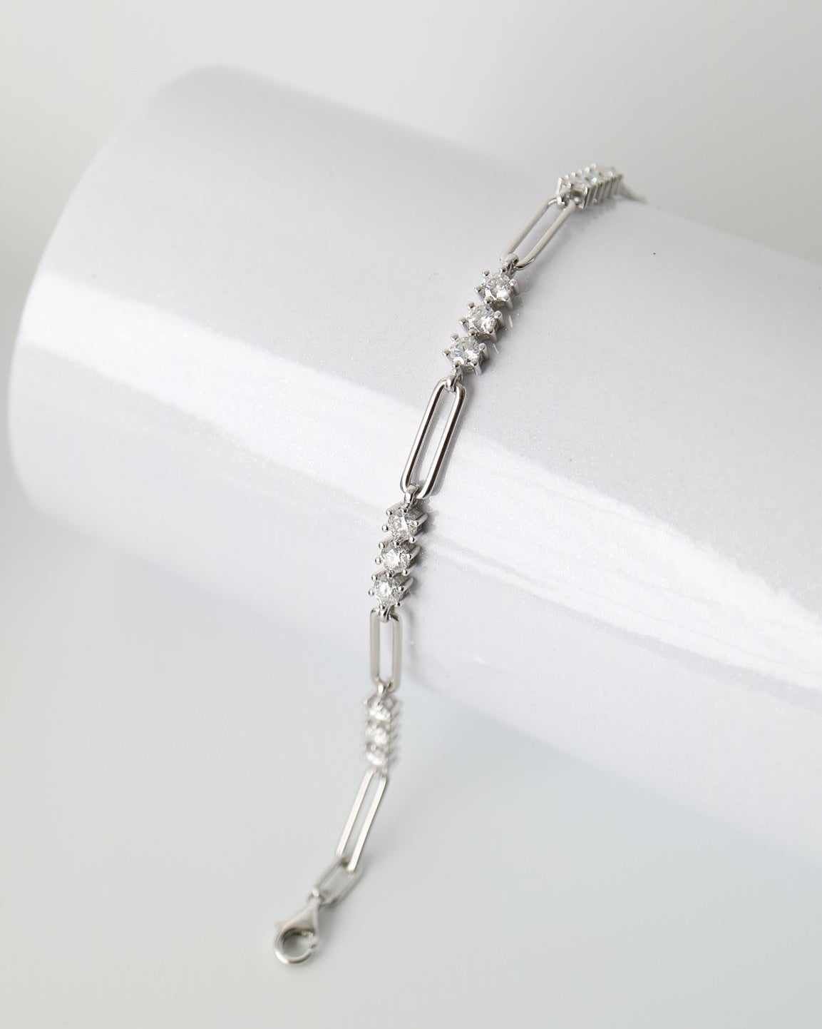 A silver-toned link bracelet with clear crystal bead accents, displayed on a white cylindrical stand against a light gray background.