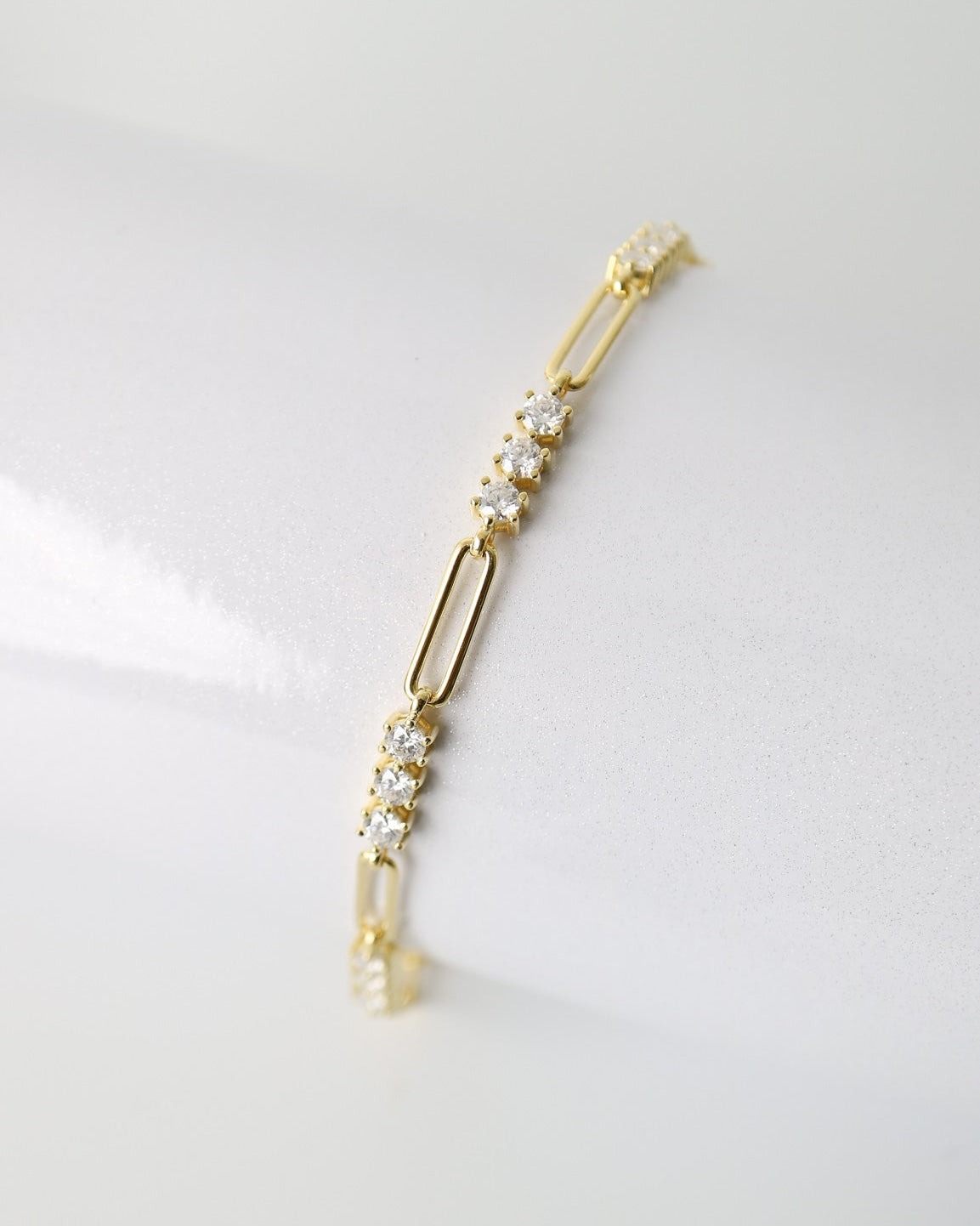A delicate gold paperclip chain bracelet with small clear crystal clusters, displayed on a clean white surface.