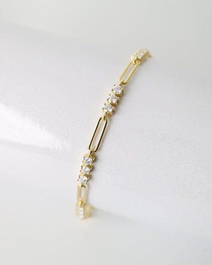 A delicate gold paperclip chain bracelet with small clear crystal clusters, displayed on a clean white surface.