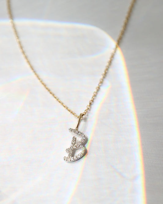 A delicate gold chain necklace with a small silver pendant adorned with clear stones, displayed on a textured white surface with soft light leaks.