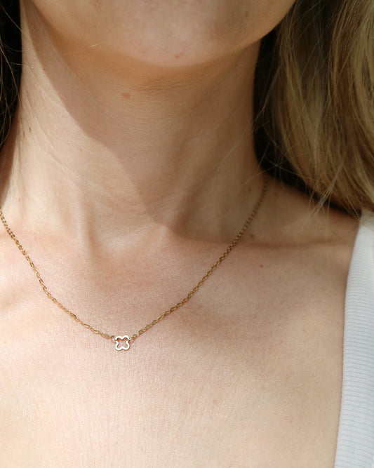 A close-up of a person's neck and upper chest wearing a delicate gold chain necklace with a small interlocking double-C pendant, styled with a white ribbed tank top.