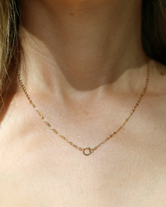 A delicate gold chain necklace with a small, minimalist circular ring pendant, shown worn on a model's neck.