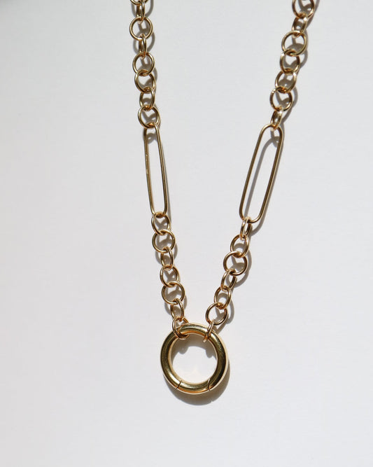 A gold-toned chain necklace featuring a large open circular ring pendant and elongated paperclip-style links, displayed against a plain white background.