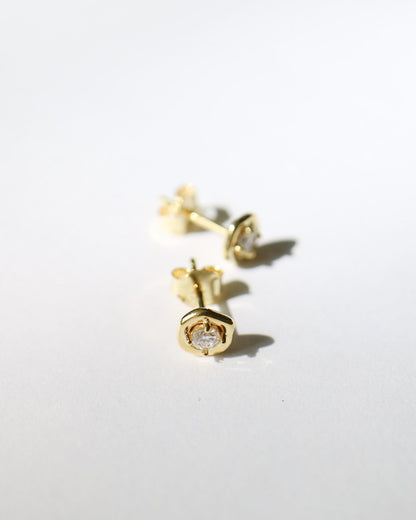 A pair of small gold stud earrings with clear gemstones, photographed on a plain white background with soft shadows.