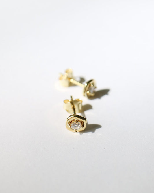 A pair of small gold stud earrings with clear gemstones, photographed on a plain white background with soft shadows.