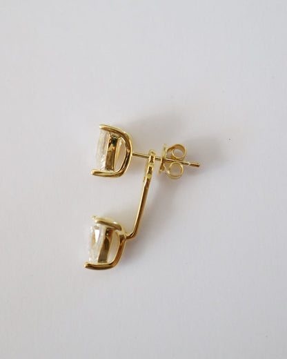 A pair of gold-toned drop earrings with curved, openwork top sections and clear faceted stones, shown on a plain light gray background.