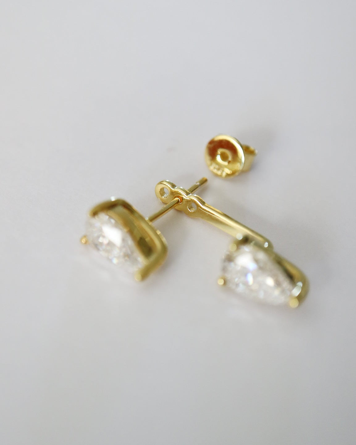A pair of gold stud earrings with clear pear-cut gemstones, shown on a plain light gray background.