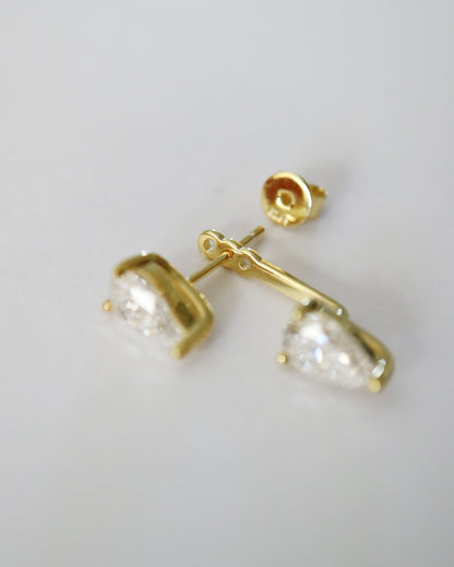 A pair of gold stud earrings with clear pear-cut gemstones, shown on a plain light gray background.