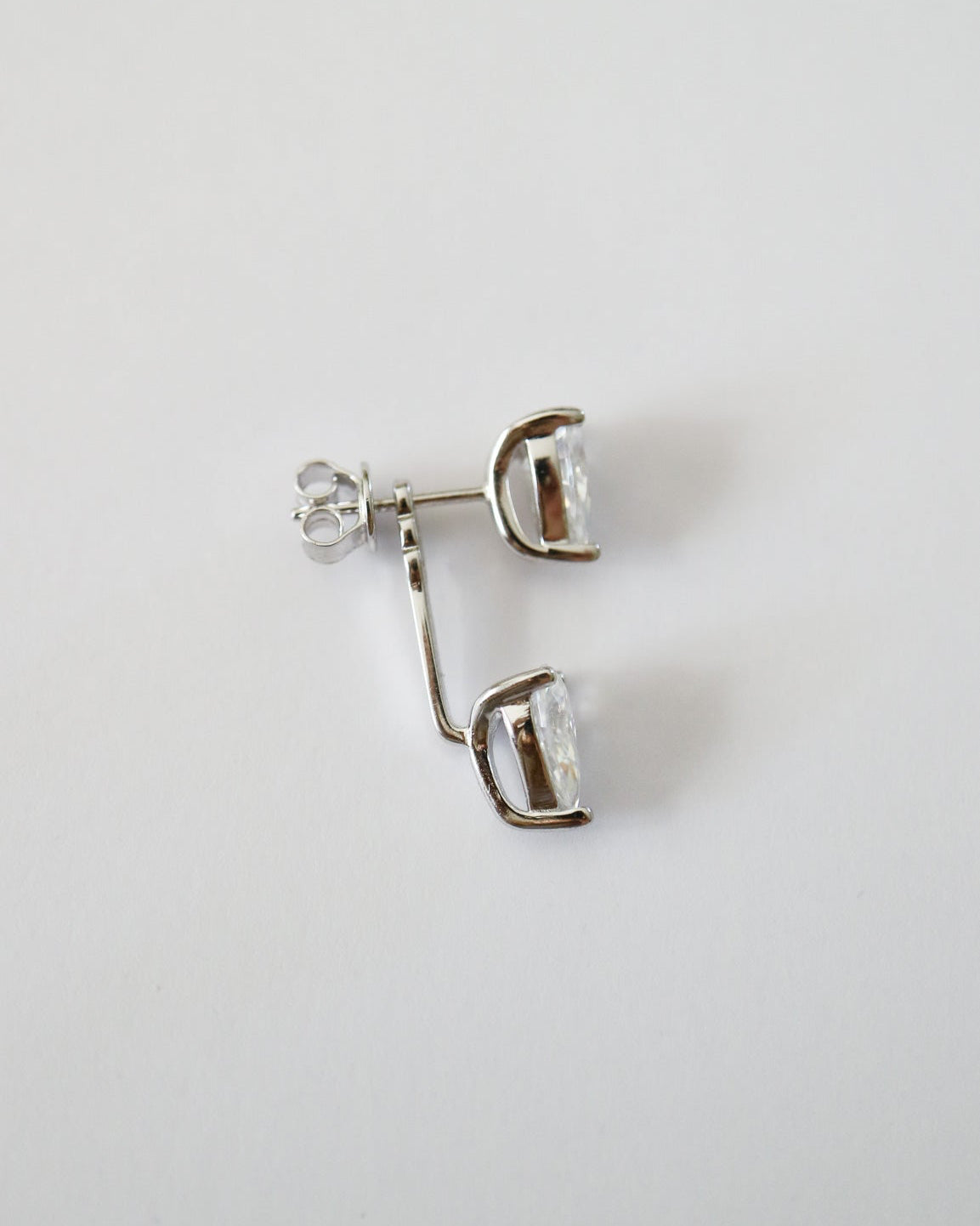 A pair of silver-toned stud earrings with clear faceted gemstones, shown on a plain light gray background.