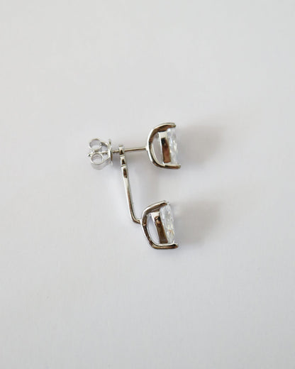 A pair of silver-toned stud earrings with clear faceted gemstones, shown on a plain light gray background.