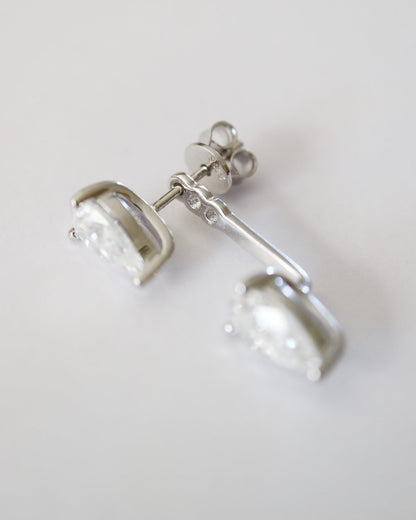 A pair of silver-toned drop earrings with clear faceted gemstones, shown on a plain light gray background.